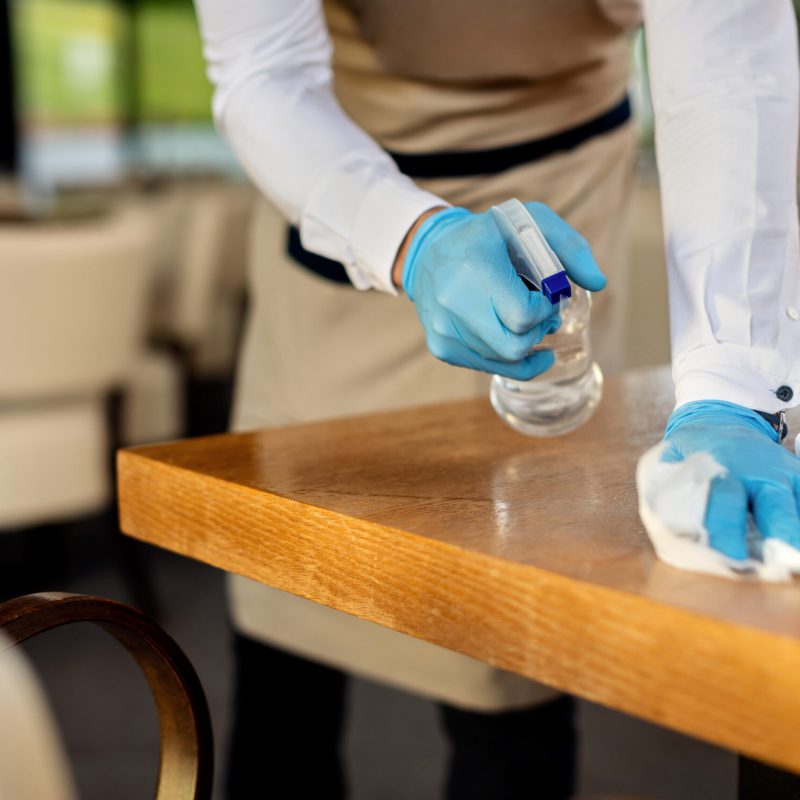 Close-up of waiter spraying cafe tables with disinfectant due to coronavirus epidemic.